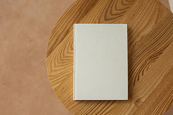 A minimalist white book rests on a textured wooden table, offering ample copy space. HD wallpaper