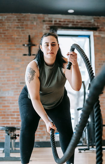 Determined woman exercising with battle ropes at the gym for endurance and strength. HD phone wallpaper