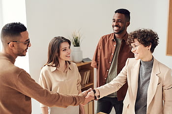 Four colleagues smiling and shaking hands in a bright office setting. HD wallpaper