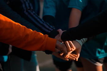 A close-up of diverse hands stacked together outdoors, symbolizing teamwork and unity. HD wallpaper