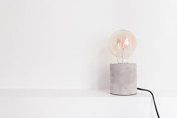 Close-up of an incandescent light bulb on a modern concrete base against a white background. HD wallpaper