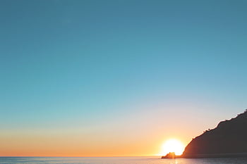 Stunning sunrise over a calm ocean with a silhouetted coastline, offering a peaceful start to the day. HD wallpaper