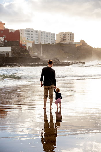 A touching family moment of a father and child walking hand in hand on a sunset beach. HD phone wallpaper