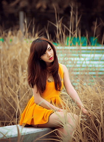 Portrait of a young woman in a vibrant dress seated outdoors, exuding elegance. HD phone wallpaper