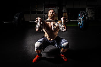 A tattooed man performing a heavy barbell squat in a gym for strength training. HD wallpaper