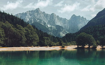 A breathtaking view of a tranquil lake surrounded by lush forests and towering mountains under a que sky. HD wallpaper