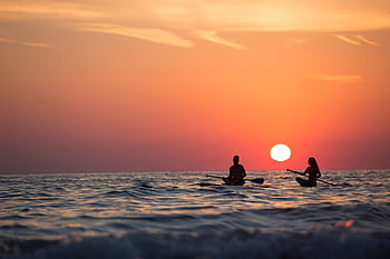 Silhouette of a couple paddleboarding on the ocean during a stunning sunset, capturing romance and adventure. HD wallpaper