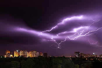 An electrifying lightning storm illuminates a modern city skyline at night, showcasing nature's power. HD wallpaper