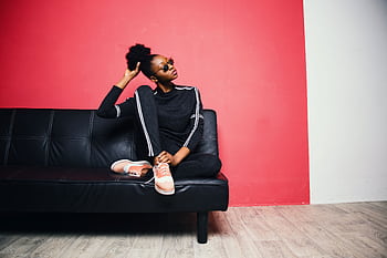 Fashionable young woman in casual wear sitting on a black sofa against a red wall. HD wallpaper