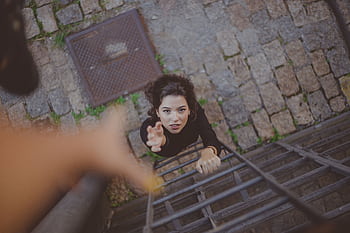 Woman climbs iron ladder outdoors, reaching for help with determination. HD wallpaper