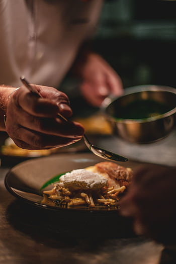 Chef artistically adds sauce to a gourmet dish in a professional kitchen setting. HD phone wallpaper