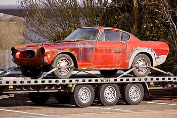 A worn-out, rusty vintage car secured on a flatbed trailer, outdoors under daylight. HD wallpaper
