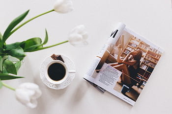 Top view of a coffee cup, flower vase, and magazine on a white table, perfect for relaxation. HD wallpaper