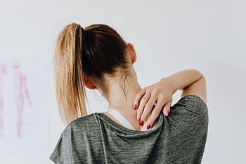 A woman in casual clothing holds her neck, indicating pain or discomfort. HD wallpaper
