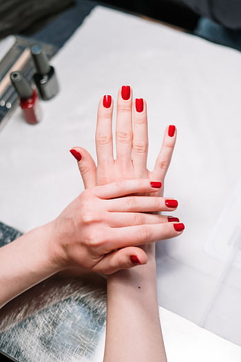 Close-up of elegant red nail polish on hands in a salon setting, showcasing modern manicure art. HD phone wallpaper