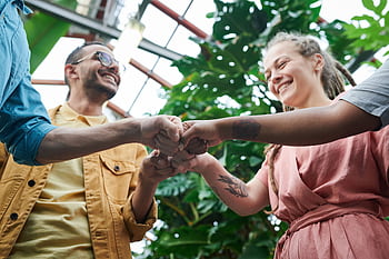 A group of young adults celebrating teamwork with a fist bump in a lush outdoor setting. HD wallpaper