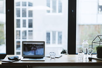 Sleek office desk setup featuring a laptop, glass of water, and open window view. HD wallpaper