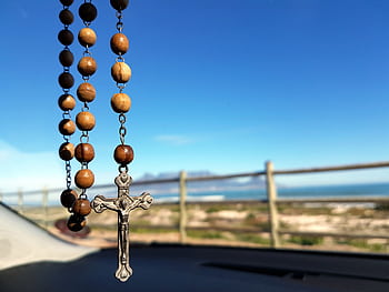 A wooden rosary with a crucifix hangs inside a car, overlooking a scenic ocean view. HD wallpaper