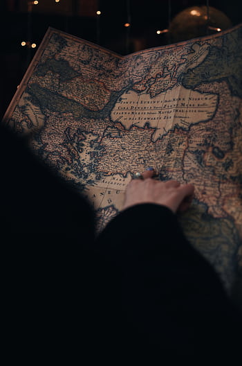 A person examining a detailed vintage map in a dimly lit environment, evoking curiosity and adventure. HD phone wallpaper