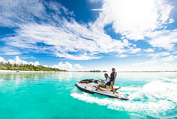 Couple enjoying a thrilling jet ski ride on crystal clear waters under a bright sky in Maldives. HD wallpaper