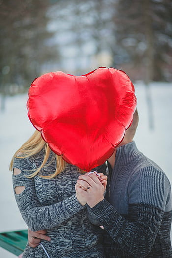 A couple embraces behind a heart-shaped balloon outdoors, depicting love and romance. HD phone wallpaper