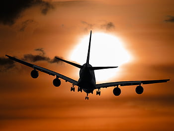 Dramatic silhouette of an airplane flying against a vibrant sunset sky. HD wallpaper