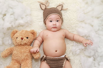 Cute baby posing with a teddy bear in a knitted outfit, exuding charm and innocence. HD wallpaper