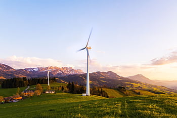 A wind turbine stands tall against a mountainous backdrop under a vibrant sky at sunset. HD wallpaper