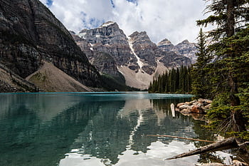 Stunning lake with mountain reflections and pine trees under clouded sky. HD wallpaper