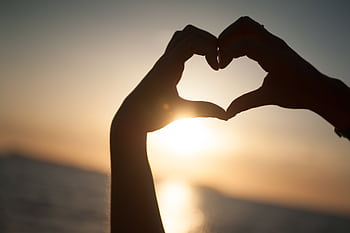 Silhouette of hands forming a heart shape against the setting sun on a beach in Spain. HD wallpaper