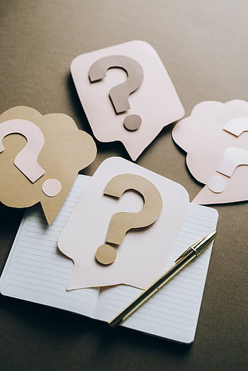 Artistic paper question marks on an open notebook with a pen, symbolizing curiosity and creativity. HD phone wallpaper