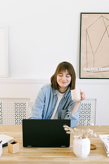 Woman in a home office setting, smiling with a coffee cup near a laptop. HD phone wallpaper