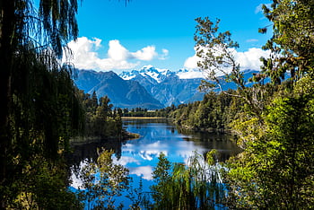 Stunning view of a clear lake surrounded by snow-capped mountains and lush forest. HD wallpaper