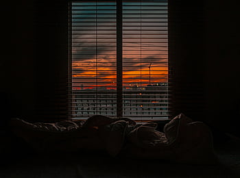 Cozy bedroom with a view of a vibrant sunset through window blinds. HD wallpaper