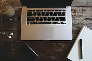 Top-down view of a laptop, heads, notebook, and iced coffee on a wooden desk. HD wallpaper