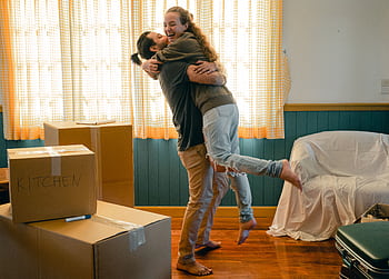 A joyful couple embracing amidst moving boxes in their new home, celebrating a new beginning. HD wallpaper