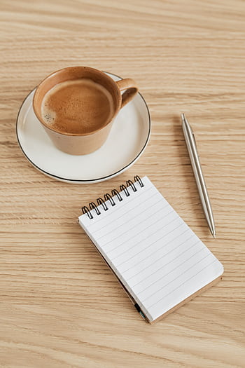 Stylish coffee break setup featuring a coffee cup, notebook, and pen on a wooden table. HD phone wallpaper