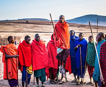 A group of Maasai men in vibrant traditional attire performing a cultural jumping dance outdoors. HD wallpaper