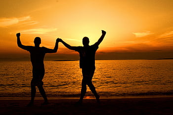 Silhouette of a joyful couple dancing on a beach at sunset, capturing the essence of happiness and romance. HD wallpaper