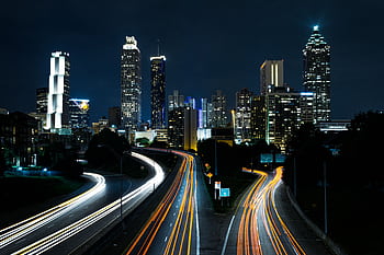 A vibrant cityscape at night showcasing light trails on the highway beneath towering skyscrapers. HD wallpaper
