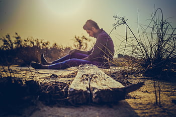 A man sits alone on sandy terrain at sunset, capturing solitude in nature's calm. HD wallpaper