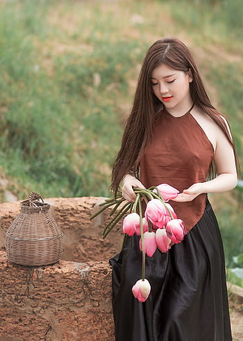 An elegant young woman holding pink tulips in a serene outdoor setting, embodying natural beauty and tranquility. HD phone wallpaper