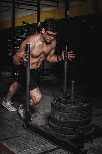 A muscular man pushes a weighted sled in an indoor gym, showcasing strength and endurance. HD phone wallpaper