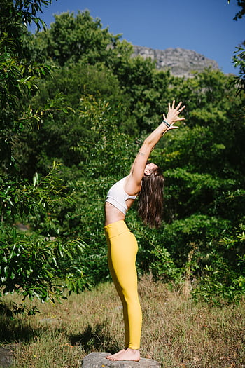 A woman in yellow leggings performs a yoga pose outdoors surrounded by green trees. HD phone wallpaper