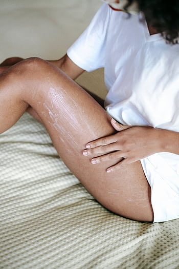 A woman gently applies moisturizing lotion to her legs, promoting a healthy skincare routine. HD phone wallpaper