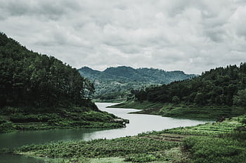 Tranquil riverside scene in Jombang, Indonesia, featuring lush forests and rolling hills under a cloudy sky. HD wallpaper