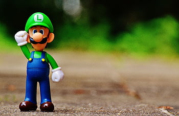 Close-up of a Luigi figurine from a videogame standing on outdoor pavement, showcasing fun and play. HD wallpaper