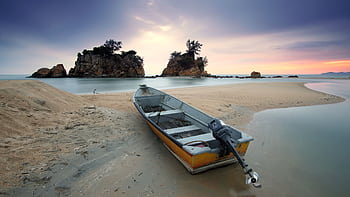 A peaceful seashore scene featuring a fishing boat on sand with a stunning dusk sky. HD wallpaper