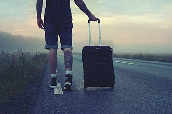 Man walking with a suitcase along a foggy road at sunrise, symbolizing adventure and travel. HD wallpaper