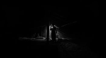 A shadowy figure explores a dimly lit, eerie attic with a flashlight. HD wallpaper